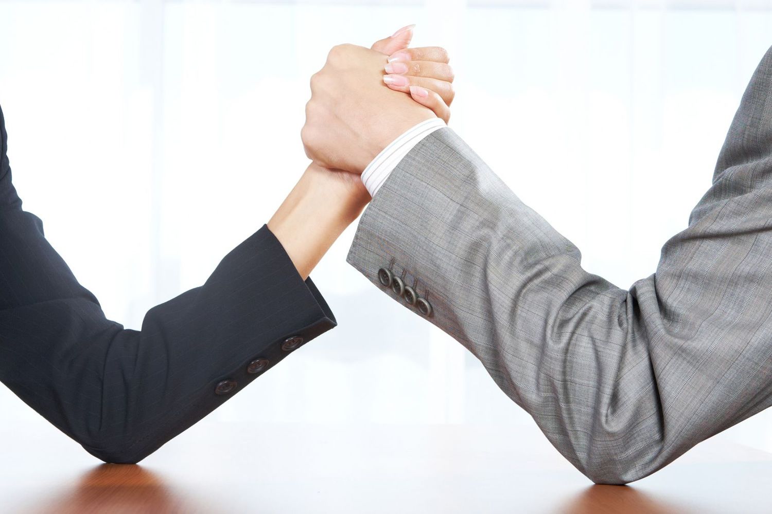Dos personas en traje de negocios compitiendo en un pulso sobre una mesa de madera