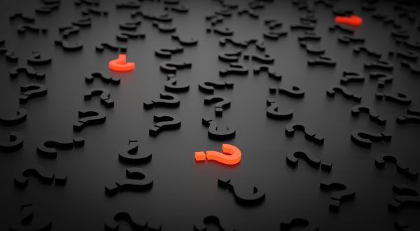 Signos de interrogación negros esparcidos sobre superficie oscura con algunos destacados en rojo brillante