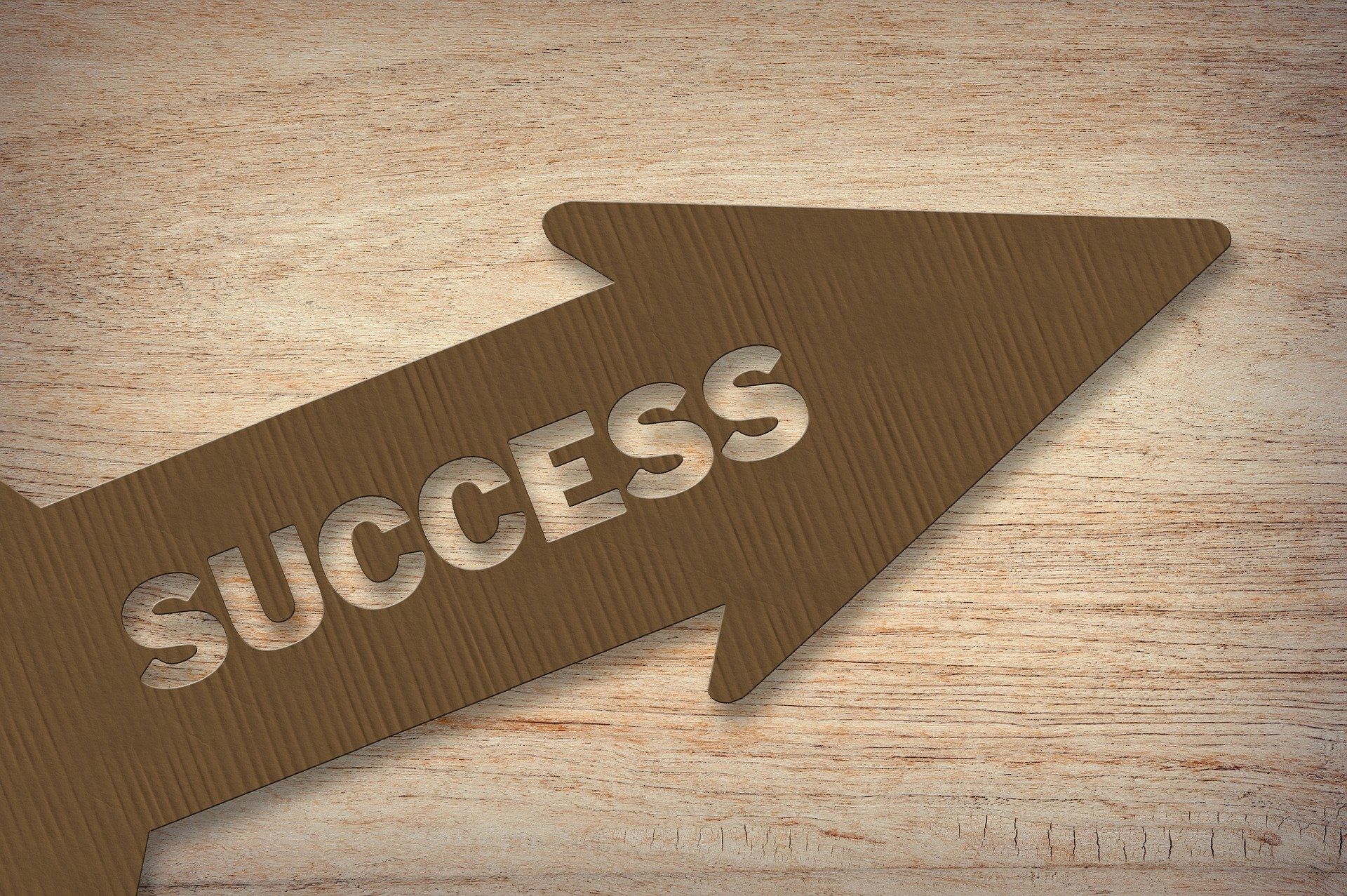 Flecha de madera con la palabra SUCCESS grabada, apuntando hacia la derecha sobre fondo de madera