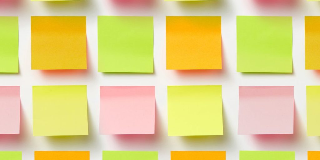 Notas adhesivas de colores en filas sobre pared blanca: amarillas, verdes, naranjas y rosas